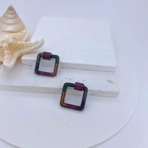 Macro shot of square rainbow zirconia screw clasps on textured white stone with starfish
