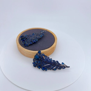 Broche plume bleu foncé avec micro-pavé de cristaux présentée sur un support en bois