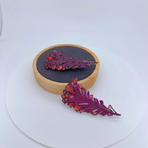 Élégante broche plume rouge rose avec zircons sertis sur un support en bois rond