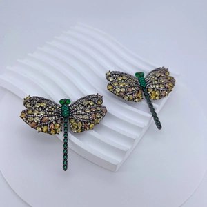 Macro detail of luxury dragonfly brooch with yellow and green crystals on black metal