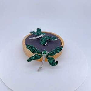 Sparkling silver dragonfly brooch set with emerald green and white zircons on wood