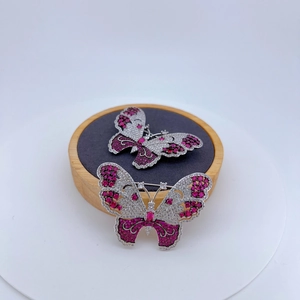 Macro detail of butterfly brooches with pavé-set zircons and magenta gemstones on wood