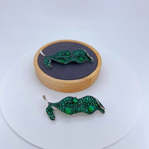 Silver leaf brooches with green zircons and emerald teardrop gems on a wood stand
