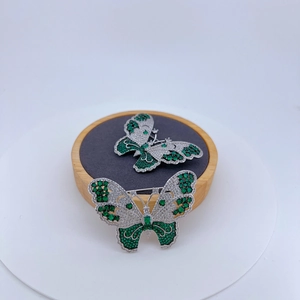 Elegant silver butterfly brooch set with green and white zircons on a display stand