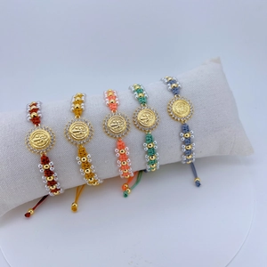 Makroaufnahme bunter geflochtener Armbänder mit goldenen Jesus-Münzen und Zirkonia-Steinen
