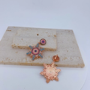 Détail de boucles d'oreilles flocon en or rose avec zircons multicolores sertis