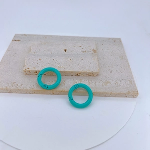 Detailed view of turquoise lacquered copper spring rings on a beige travertine surface