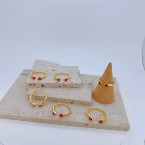 Detail van gouden open ringen met rode hartvormige zirkoon op beige travertijnstenen