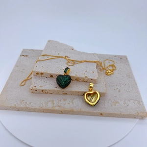 Détail du pendentif cœur avec zircons verts et chaîne dorée sur pierre naturelle