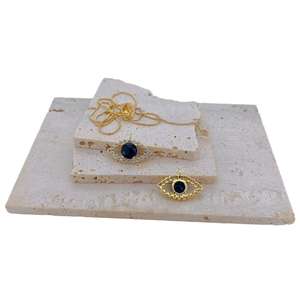 Gold evil eye necklace with blue gemstone and zircon inlay on beige stone background