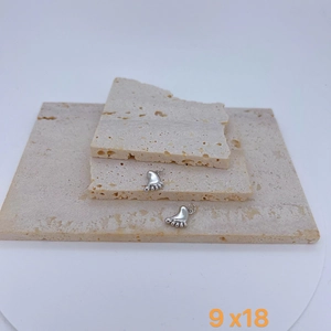 Detailed close-up of 9x18mm silver foot-shaped pendants on minimalist stone display