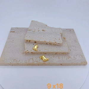 Detail of gold-plated feet pendants 9x18mm displayed on textured beige stone surface