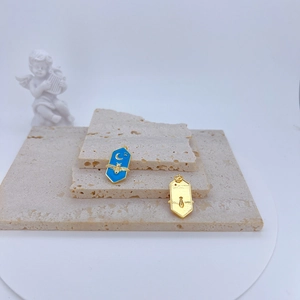 Close-up of sky blue enamel bee pendant and gold keyhole charm on textured stone blocks