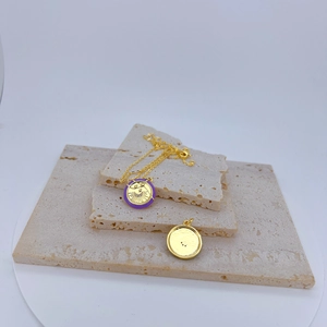 Detail of gold pendant necklace with purple enamel sun motif on travertine stone