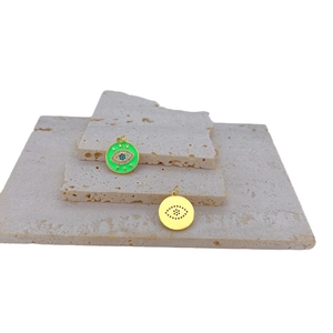 Goldene Evil Eye Anhänger mit grüner Emaille und Zirkon auf strukturiertem Steinboden