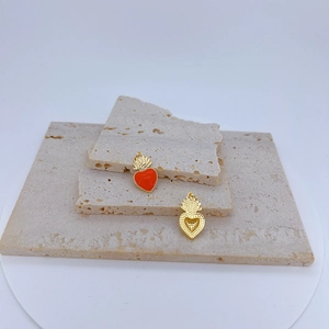 Detalle de colgantes de corazón en esmalte rojo con corona dorada sobre piedras beige