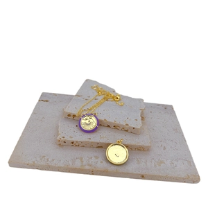 Gold-plated necklace with purple enamel moon pendant on stacked travertine stone display