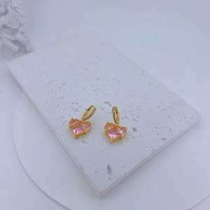 Detail of gold-plated heart earrings with pink zircon stones on marble display