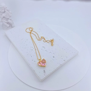 Close-up of a gold necklace with pink heart-shaped crystal on white stone
