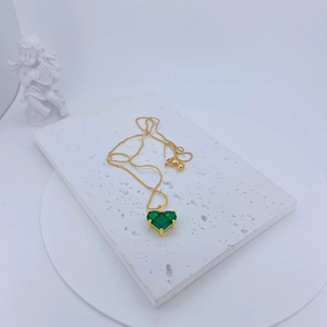 Close-up of a gold necklace featuring a heart-shaped green zircon on a stone pedestal