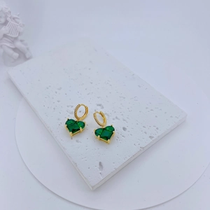 Detail of gold-plated hoop earrings featuring deep green heart-shaped gemstones