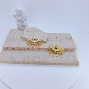 Macro detail of gold-plated evil eye charms with white enamel and micro-set zircon