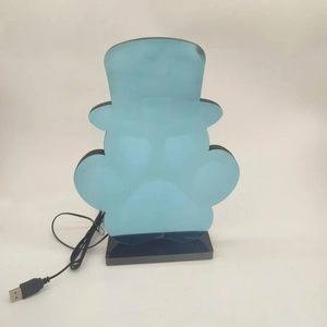 Blaue Charakter-Spiegelleuchte mit USB-Kabel und schwarzem Sockel auf schlichtem Hintergrund