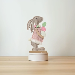 Detail of Easter bunny figurine made of felt and wood holding three colorful eggs on a stand