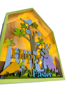 Detailed laser-cut wooden Easter house light featuring rabbits and warm LED lighting effect