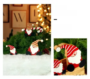 Close-up of wooden Christmas gnome hanging ornaments with red striped hats on pine branches