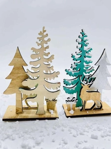 Detail of laser-cut wooden Christmas trees and reindeer ornaments on snowy white background