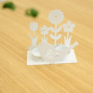 Detail of white metal tea light holder with bird and floral paper-cut art motifs