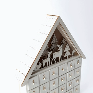 Detailed laser-cut reindeer and forest motifs atop a 24-drawer wooden advent calendar house