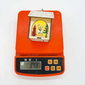 Détail d'une maison de Noël LED en bois affichant un poids léger de 34,8g sur balance