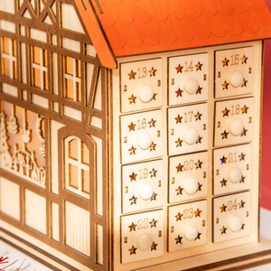 Detail of wooden advent calendar house featuring numbered drawers with star cutouts
