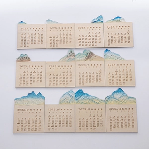 Close-up of 12-month 2023 wooden calendar cards with blue watercolor mountain scenery