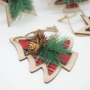 Detail of wooden Christmas ornament with red plaid fabric, pine needles, and pinecones