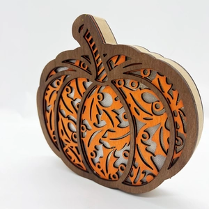 Detail of laser-cut wooden pumpkin decor with orange filigree and silver glitter layers