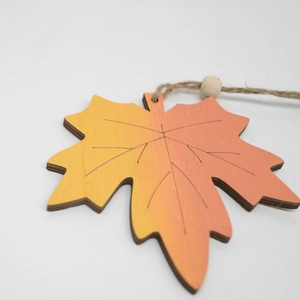 Detail of wooden maple leaf pendant with orange gradient and natural jute twine hanging