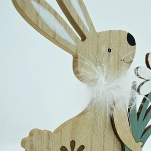 Close-up of wooden Easter bunny figurine featuring white feathers and a floral accent