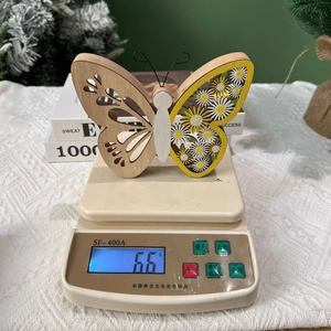 Gros plan de l'ornement papillon en bois indiquant un poids de 66g sur la balance