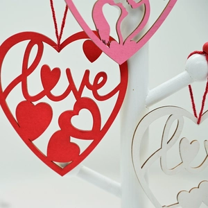 Close-up of laser-cut wooden heart ornament with hollow love text and red string