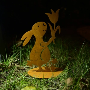 Detail of metal Easter bunny garden ornament with tulip flower on green lawn