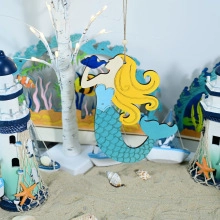 Detail view of handcrafted wooden mermaid wall hanging with nautical shell background