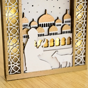 Close-up of laser-cut wooden Eid Mubarak ornament with gold glitter mosque and figures