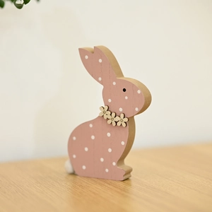 Rosa Osterhase aus Holz mit weißen Punkten und Blumenhalsband auf hölzerner Oberfläche