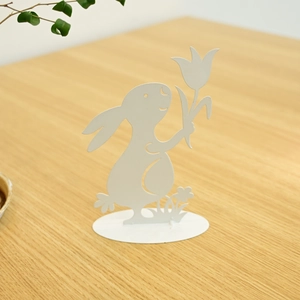 Detailed view of metal Easter bunny holding tulip on wooden surface with natural lighting