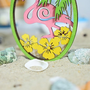 Close-up of wooden flamingo ornament with palm leaves and hibiscus flowers on beach sand
