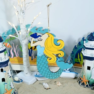 Detail of wooden mermaid ornament with painted scales hanging on a coastal decor tree