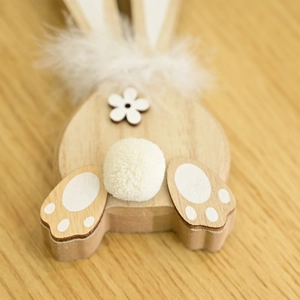 Detail of wooden bunny ornament featuring white pom-pom tail and feather neck accent